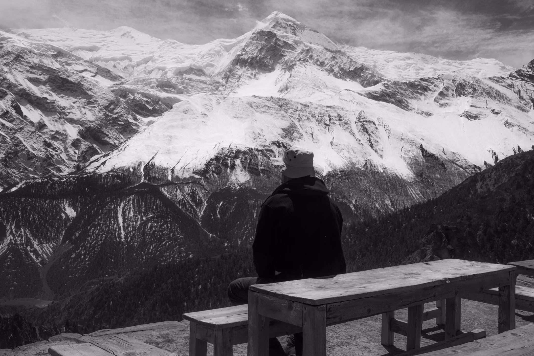 Man sitting on a bench watching a panoramic Himalayan mountain range
