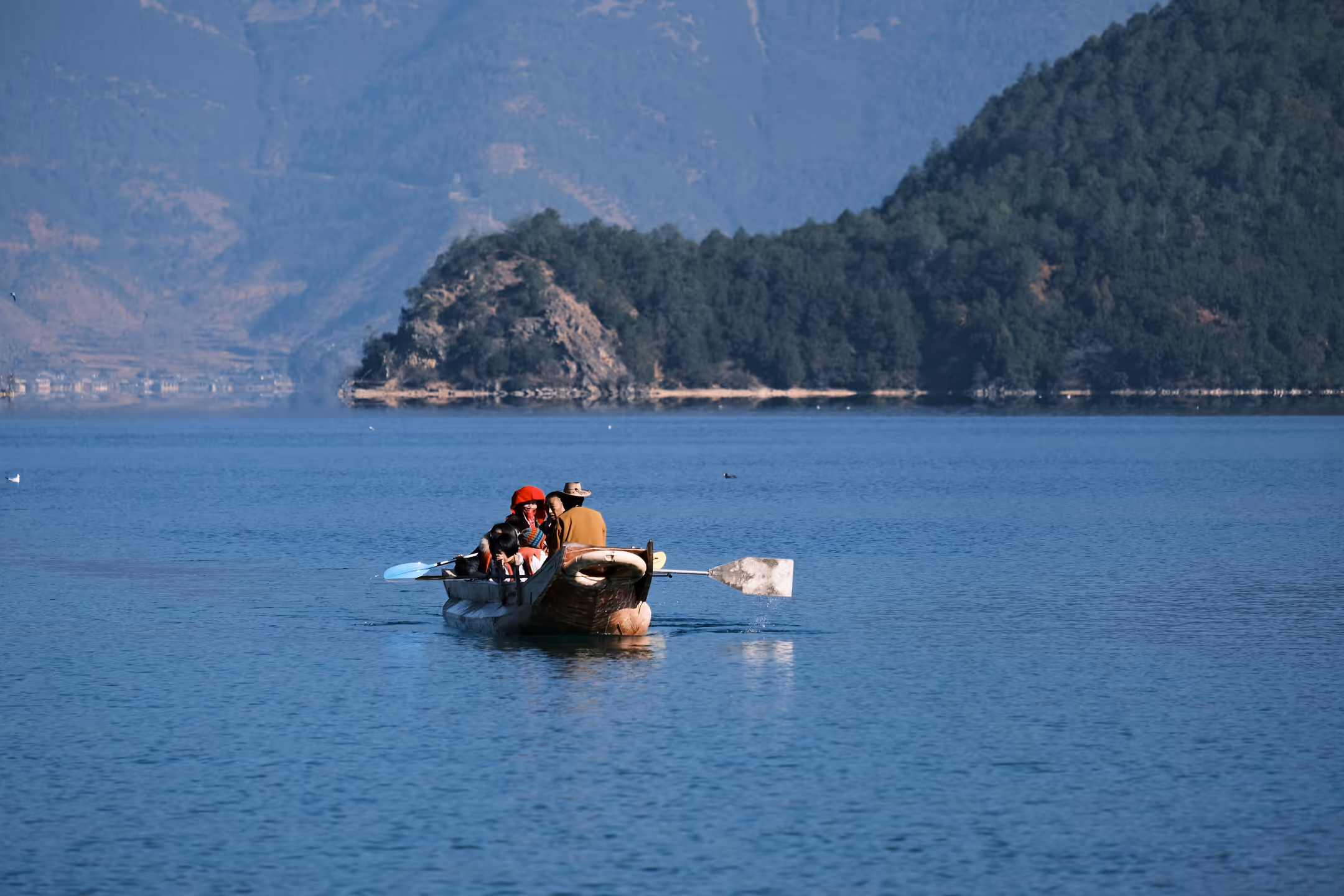 People boating on Rara Lake with forested hills in background