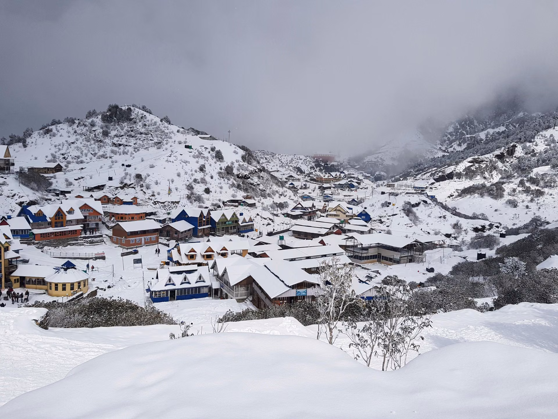 A mountain village covered in snow with Himalayan peaks behind it