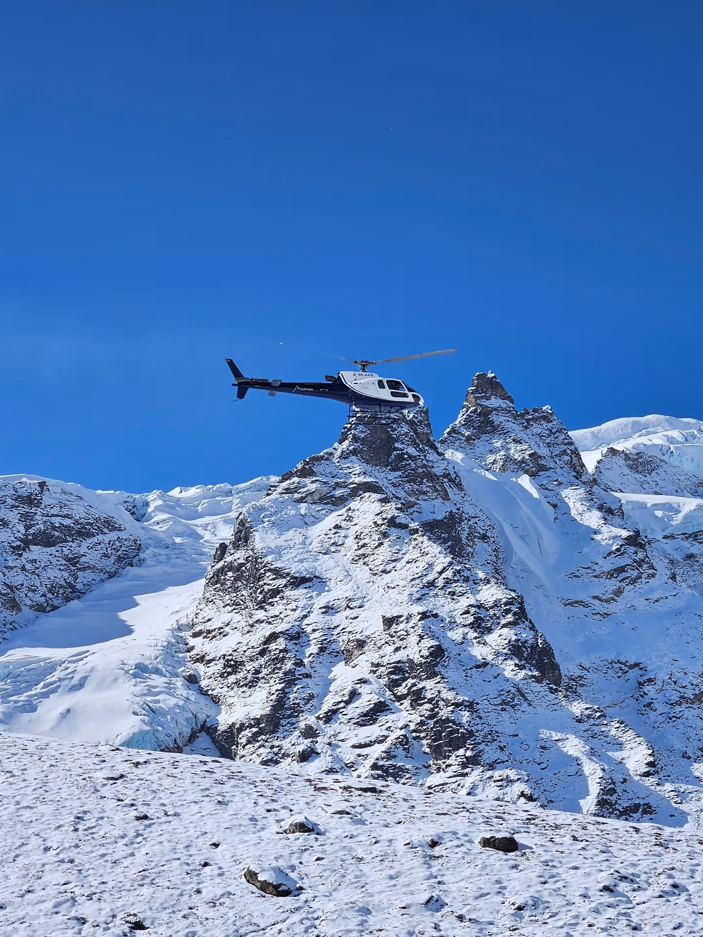 A helicopter flying in front of snowy Himalayan peaks